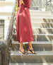 Model posing on steps while wearing an open wedge with tubular leather straps across the foot, slingback heel strap, solid wood mid-height wedge. 8