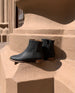 Coclico Egg Boot in Black Caviar textured leather placed on terracotta pillar.  5