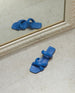 Coclico Fanima Sandal in Blu Estate leather displayed on floor with mirror reflecting shoe: a slide with squared-off toe and heel, tubular padded straps, flat feel. 5