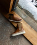 Top view of the France Boot in Caramello in the middle of a wooden doorway with a snowy landscape behind with the left shoe laying flat on the ground. 6