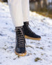 Women's legs in white pants and feet in the Heaven Shearling Boot in Black standing on snow. Front view.  7