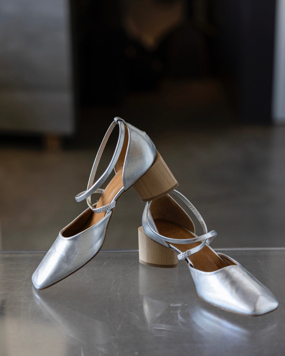 Front view of a pair of Isabel Mary Jane pumps in Milky Way on top of an acrylic table with the heel of the right shoe resting on top of the backing of the left shoe. 