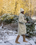 Woman outside in the snow wearing a white beanie, white coat and the Quest Boot in Tobacco.  2