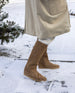 View of a women's lower legs and feet wearing the Quest Boot in Tobacco and a white coat.  5