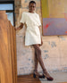 Model standing in front of a wall wearing a short white dress and the Tower Heel in Cordovan Heel.  6