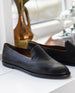 York Loafer in Black Grain Leather on a white ledge with objects in the back.  4