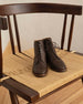 Eclair Boot in Espresso leather: a laced-up boot with a round heel, patch sole and back-zip closure - placed on woven chair.   2