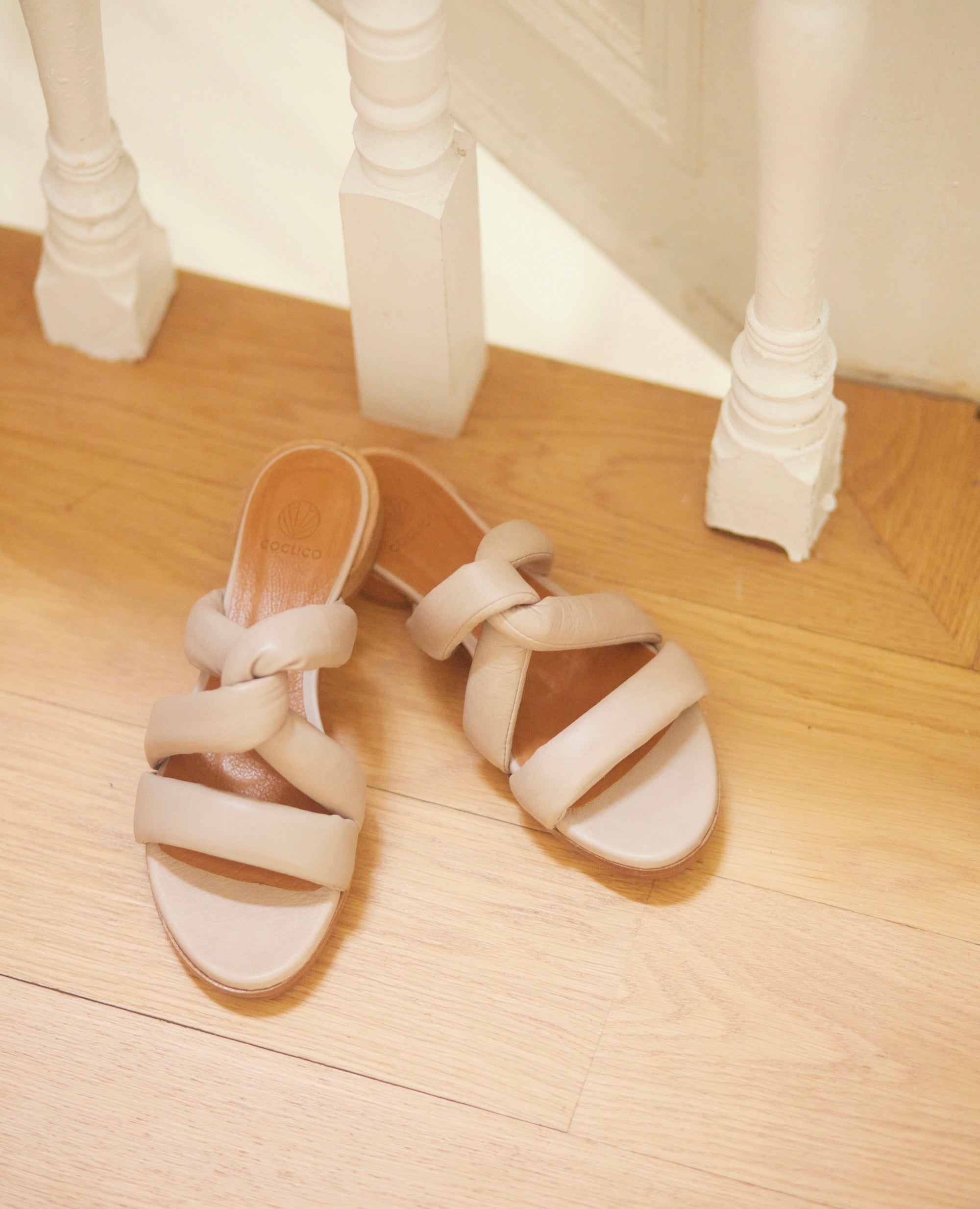 Close up of Coclico Everly Sandal in Grey Mist leather an open sandal with padded straps in a twist across the arch, raised two-part leather sole - on wood flooring.