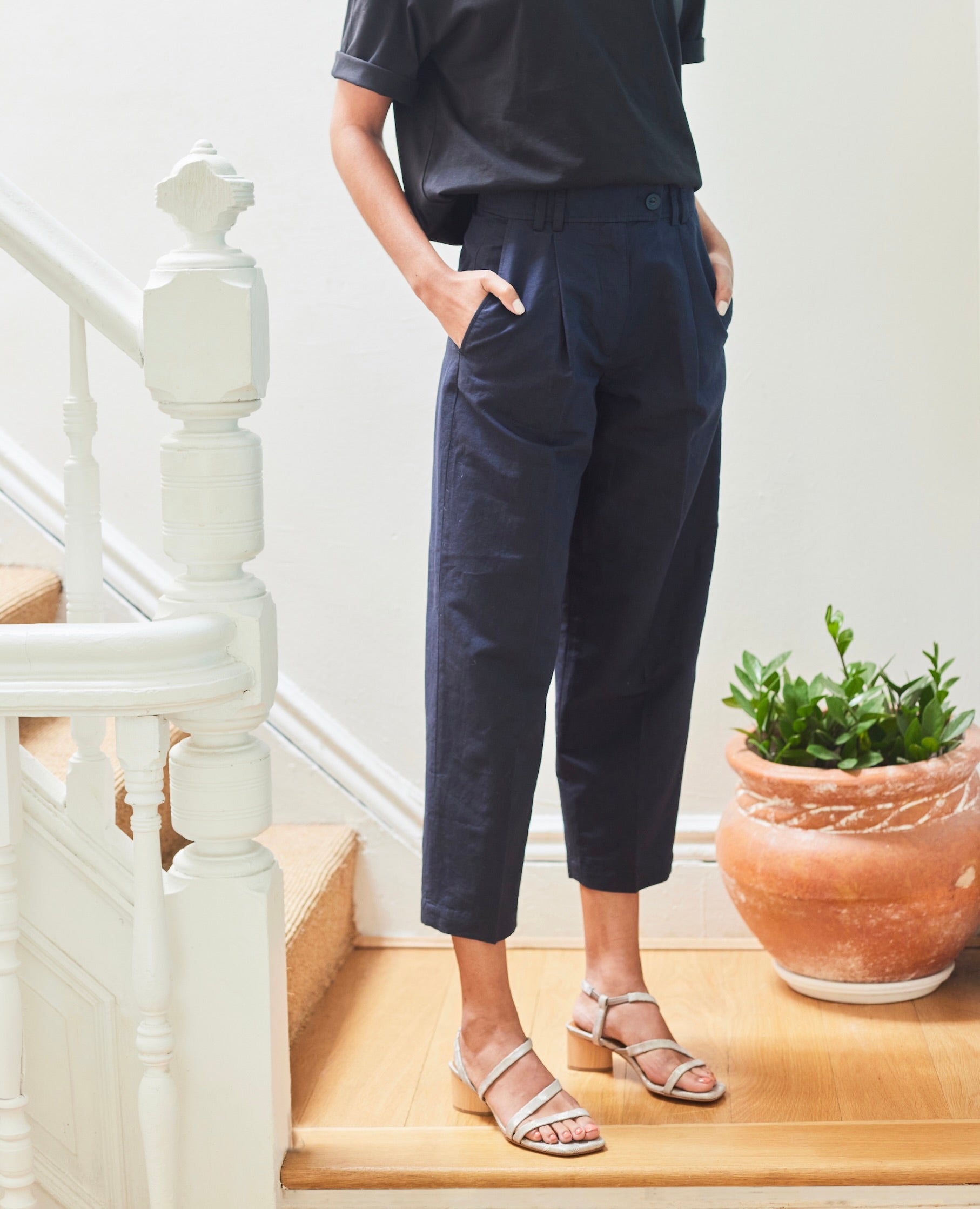 Woman modeling with hands in pocket the Coclico Shirin Heel in Platino Emboss (textured) leather: an open sandal with asymmetrical string-like straps across foot, solid mid-height wood heel.