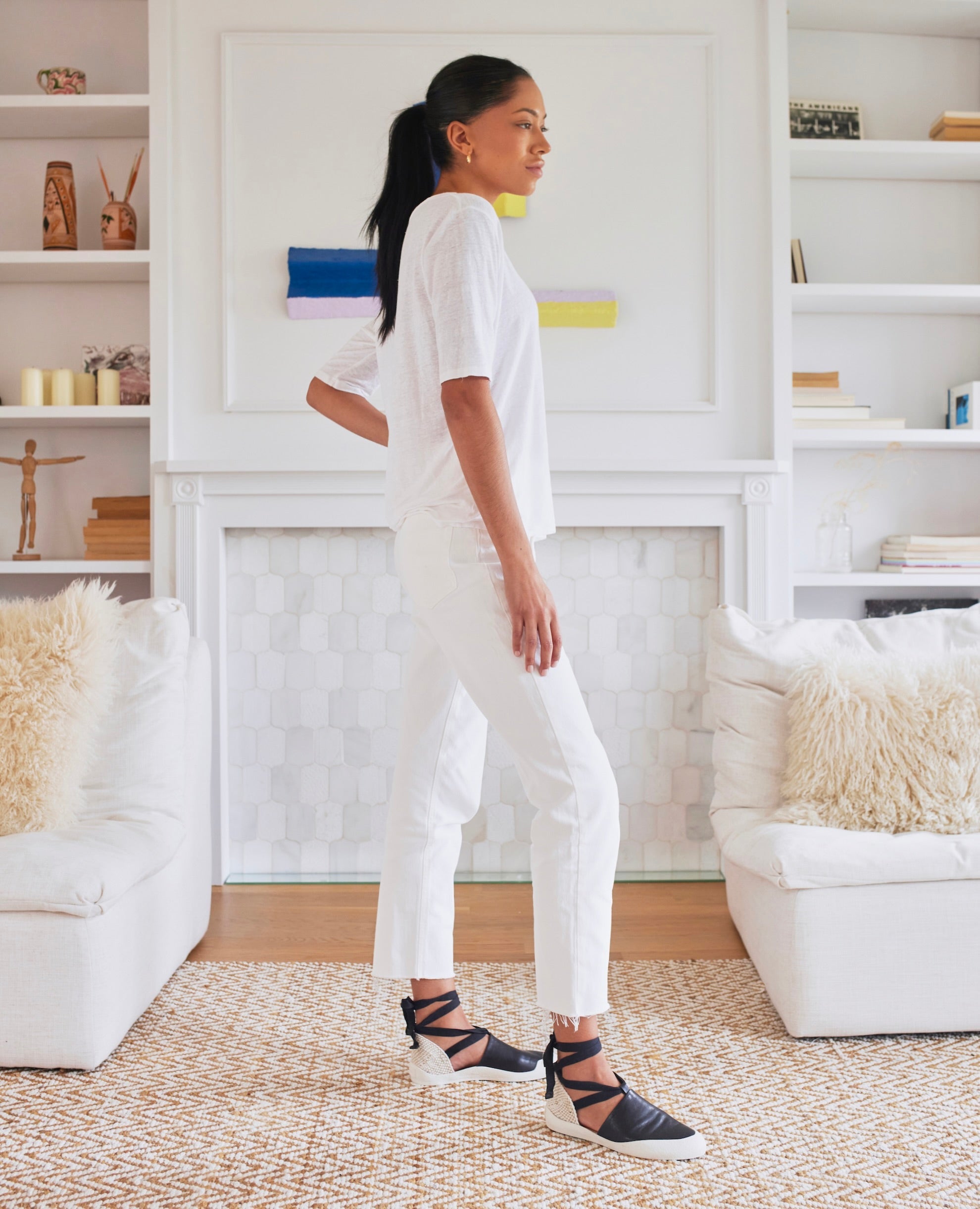 Model posing in living room in Coclico Kashm Sneaker in Black leather: unique flat-like feel sneaker with recycled rubber sole, leather upper secured with wide cotton laces that wind around the ankle.