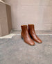 Coclico Juju Boot in Caramello leather - outdoor, angle view shot with terracotta wall in background.  5