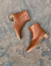 Top view, close up of the Coclico Juju Boot in Caramello leather, a minimalist boot featuring an inside zip closure, soft squared-off toe, mid-height solid wood block heel, mid-height shaft - on stone flooring.  6