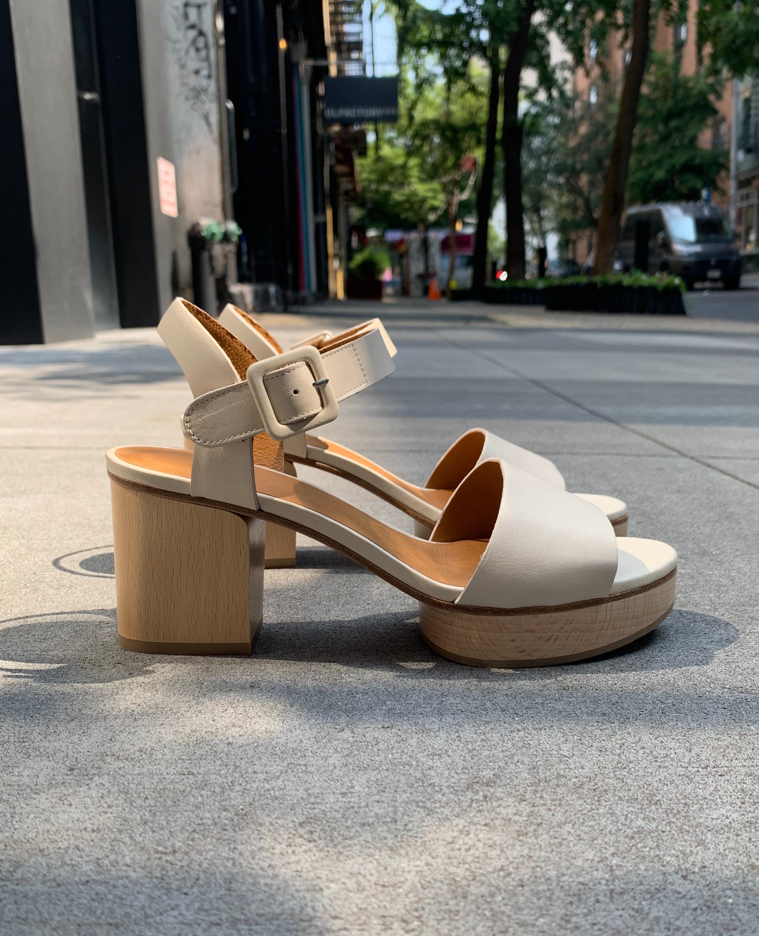 Outdoor, side view shot of Coclico Riviera Clog in Greige (off-white) leather: quarter-strap, wide front band, buckle closure, with a solid wood platform to match the solid wood mid-height heel.
