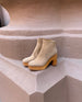 A modern, minimalist clog with a 3.5 inch solid wood heel, angled topline and back zip closure place on a large terracotta pillar.  5