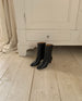 Wakame Boot in Black Leather against a white armoire.  5
