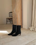 Wakame Boot in Black Leather placed on wooden flooring.  4
