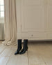 Wakame Boot in Black Leather in front of an armoire . 3