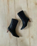 Wakame Boot in Black Leather placed on its side against a wooden flooring. 7