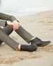 Hands, legs, and feet of a woman sitting on the beach wearing a suit and the Midori Boot in Black.  4