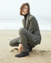 Woman wearing a black turtleneck, grey suit and Midori Bootie crouched down in the sand on a beach.  5