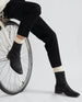 Lower legs and feet of a woman wearing black pants and the Miki Boot in Black while seated on the front of a bicycle.  5