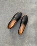 Top view close up of Coclico Gentian Flat in Black leather against a cement flooring: a closed toe slip-on flat with leather band and .5 inch rubber EVA sole. 4