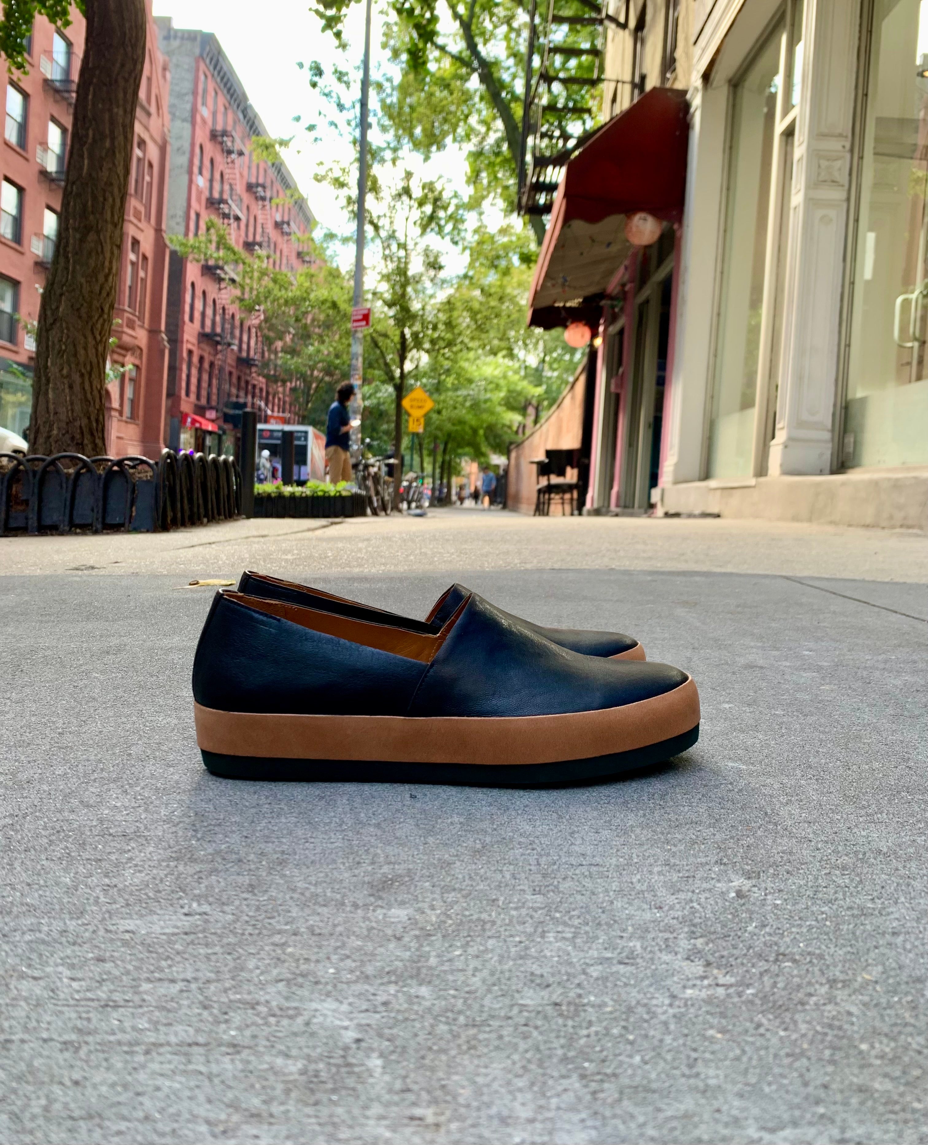 Side view shot of Coclico Gentian Flat in Black leather: a slip-on flat with leather band and .5 inch rubber EVA sole - on NYC sidewalk. 