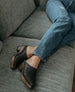 Women's legs and feet laying on a couch wearing jeans with the Kera Shearling Clog. 4