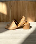Side view sunlit shot of Coclico Okolo Sandal in Mandorla leather a slingback sandal with a wide stretch leather band across the foot and a softly curved, low, solid walnut wood heel. 6