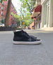 Side, floor view of the Oro Sneaker in Black placed outside a tree lined street.  5