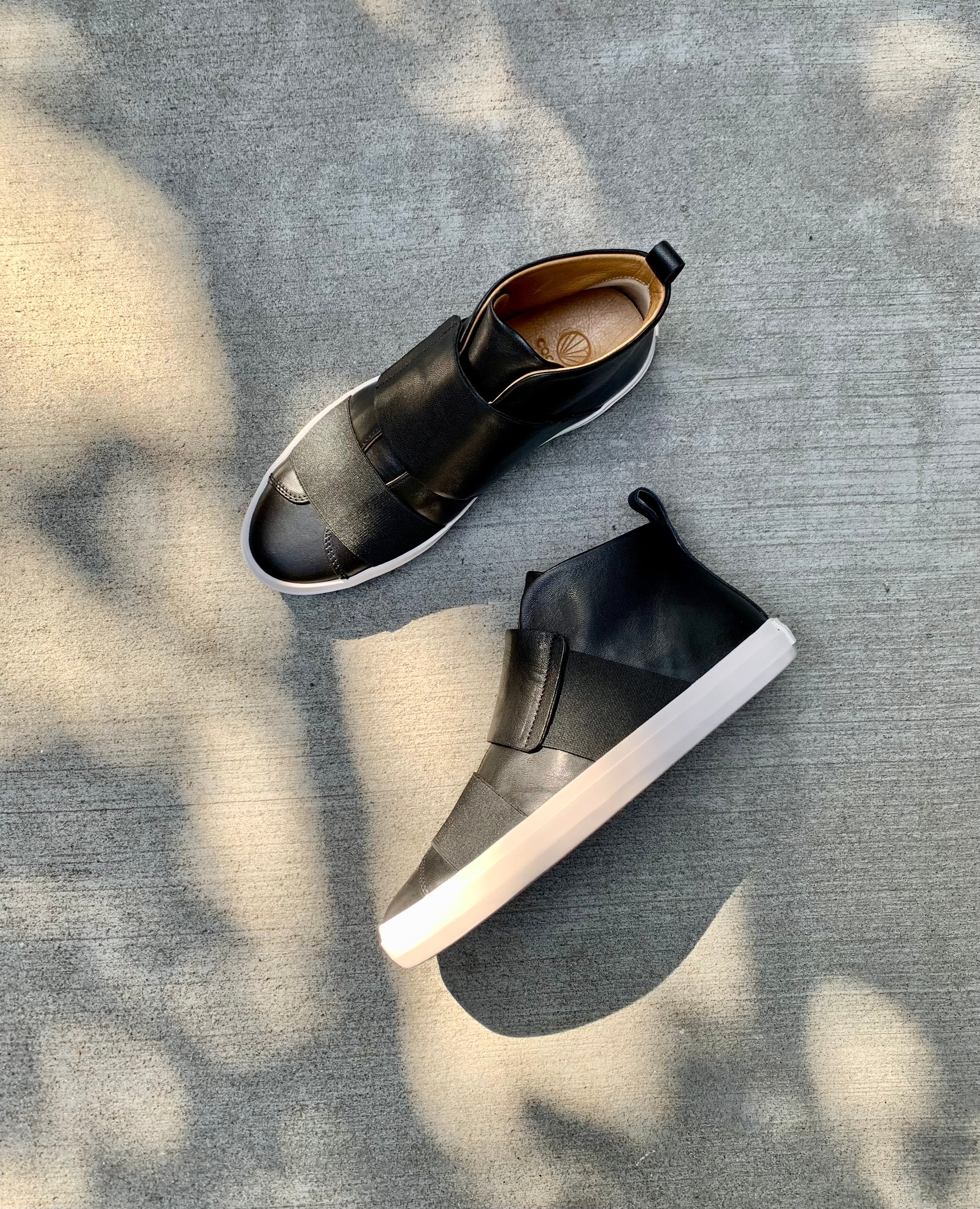 Top view of the Oro Sneaker in Black with the left lying on its side against cement flooring. 